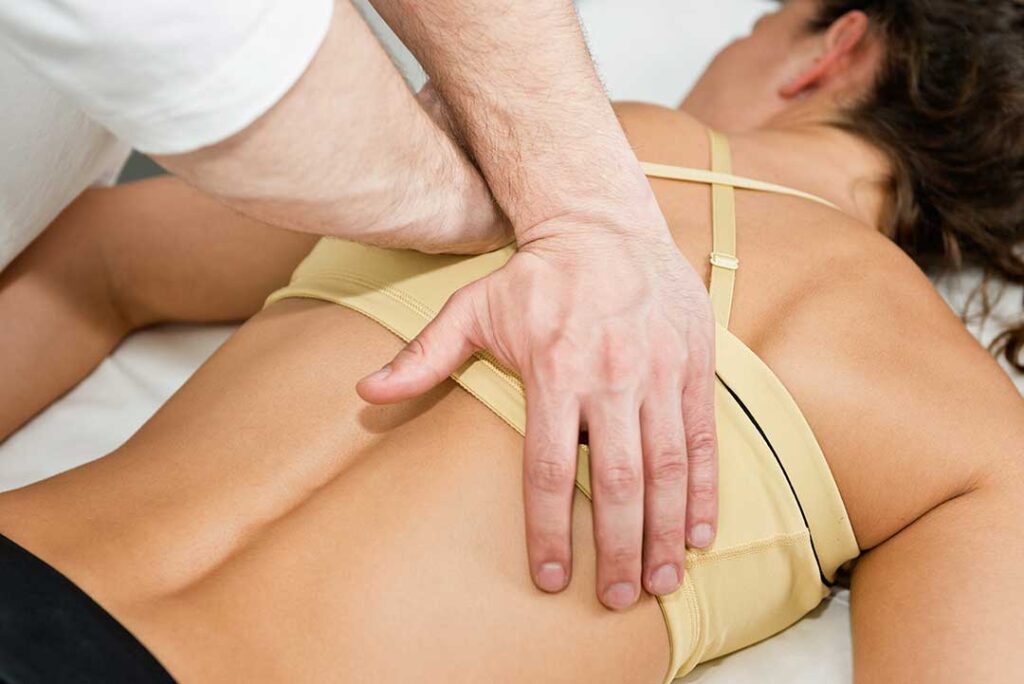 A clinician discusses spinal mobility with an adult seated in an examination room.